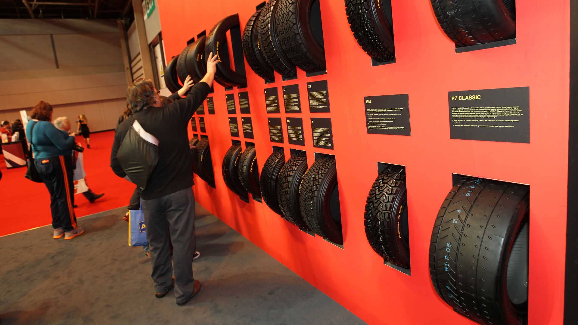 man touching a tyre on a display wall of tyres